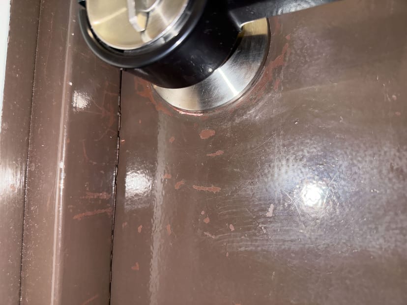 築古ドアの表面。ドアノブ周辺のペンキが剥がれてサビが露出している